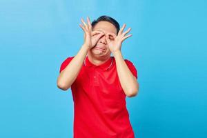 retrato de jovem asiático mostrando sinal de ok com os dois dedos e cobrindo os olhos sobre fundo azul foto