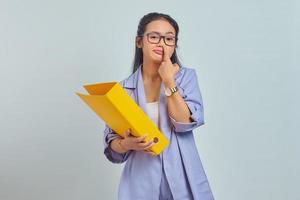 retrato de uma jovem asiática engraçada pensando em algo enquanto carregava pasta amarela e pegando o nariz isolado em fundo amarelo foto