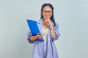 retrato de uma jovem empresária asiática alegre segurando o queixo enquanto segura a pasta de documentos isolada no fundo roxo foto