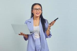 retrato de jovem asiática em pé usando laptop e segurando o celular com expressão alegre isolada no fundo branco foto