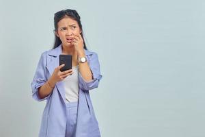 retrato de jovem mulher asiática usando telefone celular parecendo estressado e nervoso com a mão na boca roendo unha no fundo branco foto