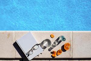 livro branco com copos e frutas ao lado da piscina foto