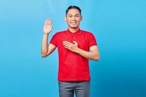 retrato de jovem asiático bonito sorrindo e mostrando o gesto de saudação para isolado no fundo azul foto