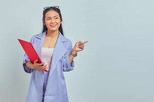 retrato de uma jovem empresária asiática sorridente de terno segurando a pasta de documentos e apontando o dedo para o espaço da cópia isolado no fundo roxo foto