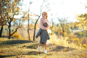 retratos de uma encantadora garota ruiva com um rosto bonito. garota posando no parque outono em um suéter e uma saia cor de coral. a menina tem um humor maravilhoso foto