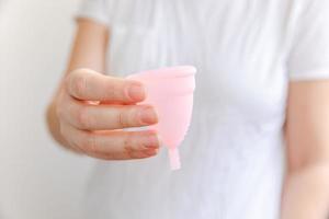 mão de uma mulher segurando o copo menstrual rosa isolado no fundo branco. mulher moderna alternativa eco ginecológica higiene no período de menstruação. recipiente para sangue na mão da menina. foto