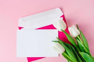 envelope com convite para férias e buquê de tulipas em fundo rosa. foto