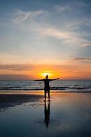 silhueta de homem stanidng na praia ao pôr do sol foto
