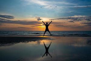 silhueta de homem pulando na praia ao pôr do sol foto