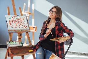 menina pintora pensativa criativa pinta um quadro colorido na tela com cores a óleo na oficina foto