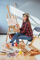 menina pintora pensativa criativa pinta um quadro colorido na tela com cores a óleo na oficina foto