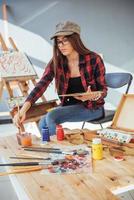 menina pintora pensativa criativa pinta um quadro colorido na tela com cores a óleo na oficina foto