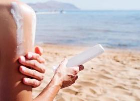 cosméticos de proteção solar. mulher caucasiana aplicando protetor solar tomando sol na praia foto