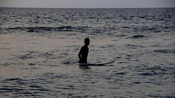 documentação de surfistas em ação ao entardecer com cor dourada e escura, desfocada e escura na praia de senggigi lombok, west nusa tenggara indonésia, 27 de novembro de 2019 foto