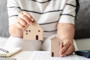 mulher está decidindo escolher casa com modelo de casa de madeira pequena, planejando comprar propriedade. escolha o que há de melhor. conceitos de empréstimo à habitação. foto