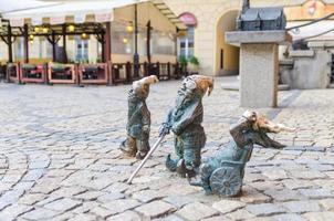 wroclaw, polônia, 7 de maio de 2019 três anões surdos, cegos com uma bengala e inválidos em cadeira de rodas, famoso gnomo em miniatura de bronze com escultura de chapéu é um símbolo de wroclaw no antigo centro histórico da cidade foto
