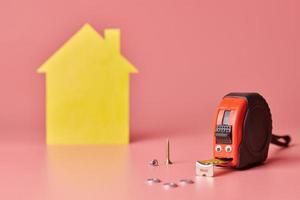 conceito engraçado de fita métrica de metal. reforma da casa. reparo em casa e conceito redecorado. figura em forma de casa amarela no fundo rosa. foto