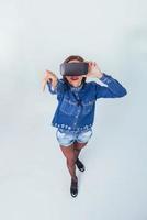 mulher bonita morena posando no estúdio, vestindo jeans, usando fones de ouvido de realidade virtual de óculos vr foto