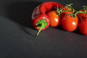 ramo de tomate e pimenta vermelha, isolado em um fundo preto foto