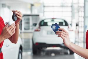 negócio de automóveis, venda de carros, negócio, gesto e conceito de pessoas - close-up do revendedor dando a chave para o novo proprietário no salão ou salão de automóveis foto