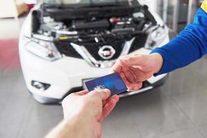 mãos de mecânico de automóveis com chave na garagem, pagamento com cartão de crédito foto