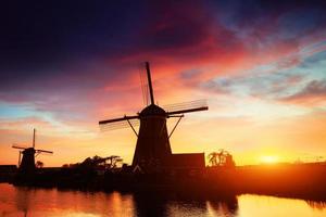 paisagem com belo moinho holandês tradicional perto de cursos de água com pôr do sol fantástico e reflexo na água. Holanda. foto