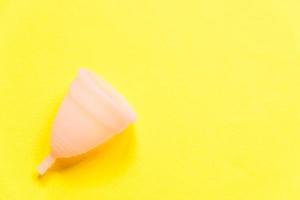 copo menstrual rosa design simplesmente minimalista isolado em fundo amarelo. mulher moderna alternativa eco ginecológica higiene no período de menstruação. recipiente para sangue. vista superior plana, copie o espaço foto