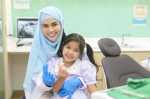 uma menina bonita tendo os dentes examinados pelo dentista muçulmano na clínica odontológica, check-up dos dentes e conceito de dentes saudáveis foto