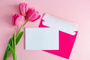 envelope com convite para férias e buquê de tulipas em fundo rosa. foto