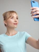 blogueira de mulher loira bonita elegante fazendo selfie com seu smartphone pela janela. tendência, tecnologia, beleza, conceito de moda foto