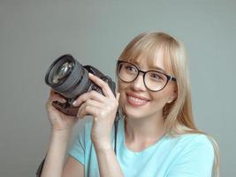 fotógrafo de mulher alegre elegante loira de óculos e segurando a câmera fotográfica. hobby, trabalho, conceito de tiro foto