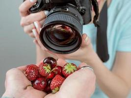 fotógrafo jovem tiro com câmera digital morangos e cereja nas mãos. close-up, tiro, hobby, comida, conceito de profissão
