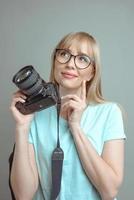 fotógrafo de mulher alegre elegante loira de óculos e segurando a câmera fotográfica. hobby, trabalho, conceito de tiro foto