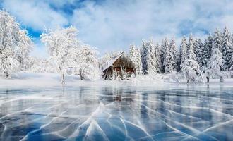 gelo azul e rachaduras na superfície do gelo. lago congelado sob um céu azul no inverno. cabana nas montanhas. névoa misteriosa. Cárpatos. Ucrânia, Europa foto