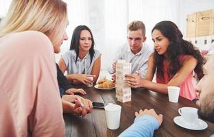 grupo de amigos criativos sentados à mesa de madeira. pessoas se divertindo jogando jogo de tabuleiro foto