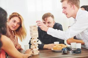 grupo de amigos criativos sentados à mesa de madeira. pessoas se divertindo jogando jogo de tabuleiro foto