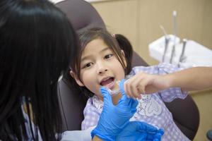 dentista feminina mostrando invisalign para uma garotinha na clínica odontológica, check-up de dentes e conceito de dentes saudáveis foto