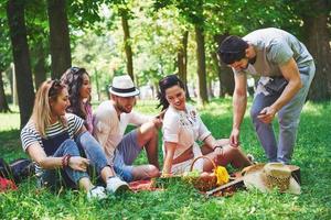 grupo de amigos fazendo piquenique em um parque em um dia ensolarado - pessoas saindo, se divertindo enquanto grelha e relaxa foto