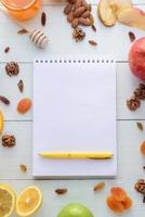caderno com caneta cercada por maçãs, kiwi, frutas secas, laranjas e maçãs. o conceito de uma dieta saudável e lista de compras. foto