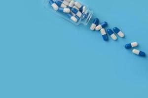 pílula de cápsulas azul e branca derramada do frasco de vidro de remédio. foto