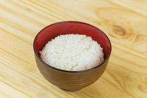 arroz de jasmim cozido em tigela branca na mesa de madeira e fundo escuro com espaço de cópia, comida de alto teor calórico, vista superior. foto