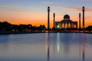 mesquita central songkhla do dia para a noite com céus coloridos ao pôr do sol e as luzes da mesquita e reflexos na água no conceito de paisagem de referência foto