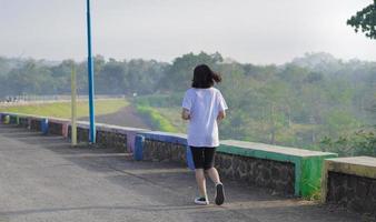 jovem fitness mulher asiática está correndo e correndo um treino ao ar livre na estrada pela manhã foto