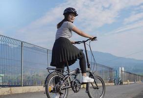 jovem mulher asiática gostando de andar de bicicleta quando parou na manhã de verão foto