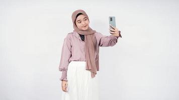 mulher bonita em hijab, agindo na câmera na frente de seu telefone bonito expressão sorridente isolada no fundo branco foto