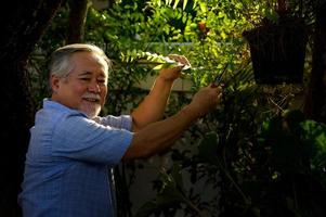 um homem idoso fica feliz em cuidar das flores e plantas no jardim da casa. foto