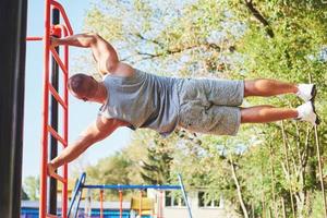 homem musculoso com belo torso se exercitando em barras horizontais em um fundo desfocado do parque. jovem fazendo pull-ups ao ar livre foto