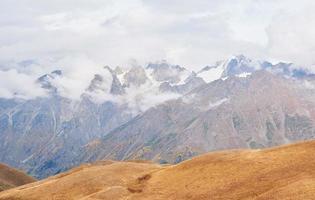 fantásticas montanhas cobertas de neve nas belas nuvens cumulus. cume caucasiano principal. tipo monte ushba meyer, geórgia foto