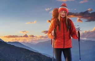 uma mulher com uma mochila descansa no topo da montanha e aprecia a vista do vale foto