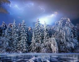 árvore mágica coberta de neve de inverno. céu dramático de tempestade. o lago de inverno está congelado na frente foto